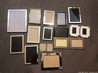 Photo showing all 15 frames laid on carpet in an arrangement, silver and gold tones, various sizes, paper placeholders inside some frames.