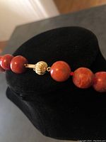 Close-up of gold ball clasp and adjacent coral beads on black bust stand