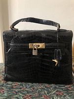 Front view of black crocodile leather handbag showing flap, handle and turn-lock closure.