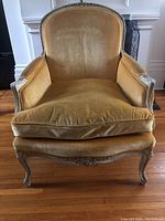 Frontal view of the Louis XV style bergere armchair showing yellow velvet upholstery, carved wooden frame, and down filled cushion.