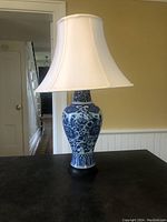 Full view of the vintage Chinese blue and white ceramic ginger jar table lamp with fabric shade on a dark table.