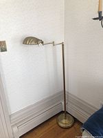 Full view of the vintage brass floor lamp standing in corner near baseboard heater, showing lamp height and base.