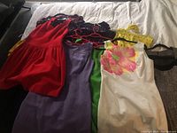 Overview of six colorful vintage dresses on hangers laid out on bed
