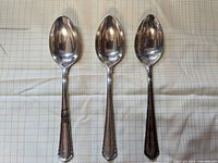 Three large silver serving spoons displayed on a patterned fabric, showing size and finish