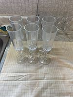 Six contemporary crystal glass flutes arranged in two rows of three on a checkered cloth surface near a kitchen sink.