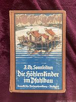 Front cover showing colored illustration of stilt houses on a lake with mountains and Gothic text