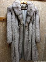 Front view of the long blue fox fur coat hung on a hanger, showing the collar, snap closure, and fur texture.