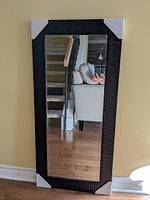 Front view of the full-length wall mirror showing the dark coffee bean brown imitation wood frame with wavy texture and the mirror reflecting a living area with sofa and staircase.