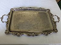 Large rectangular metal or silver plated tray showing ornate edges and handles with visible wear on the surface.