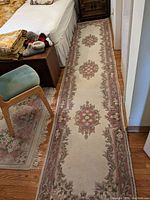Long Persian runner rug laid out on hardwood floor near bed showing full length and floral medallion patterns in cream, mauve, pink, and green.