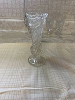 Front view of clear textured glass rosebud vase standing on gridded surface. Shows scalloped rim and patterned body.