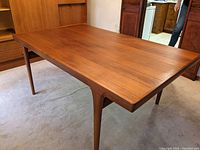 Full view of teak dining table assembled without leaves, showing tabletop and tapered legs