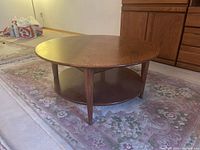 Top view of round oak coffee table showing smooth surface and wood grain, positioned on floral carpet.
