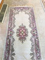 Top-down view of the Persian runner rug showing cream base and mauve floral medallion pattern with fringe at top edge.