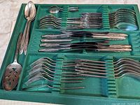 Full set of silverware including forks, knives, spoons, arranged in green velvet tray.