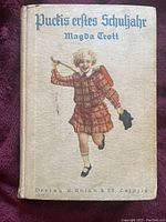 Front cover of the vintage hardcover novel showing a young girl running with a school satchel and doll, title and author printed in old German script.