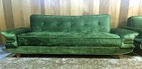 Front view of the green velour sofa in upright position against wood panel wall