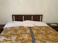 Full view of queen size bed with solid walnut wood headboard against wall, bed partially made with linens and decorative cushions.