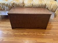Front view of wooden chest showing rectangular shape, flat top lid, and decorative base cutouts.