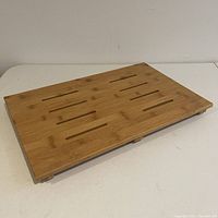 Top-down angled view of rectangular bamboo shower mat showing slotted surface design and natural wood grain.