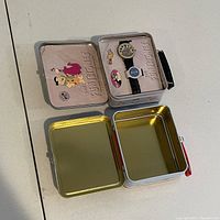 Open Flintstones mini lunchbox showing watch and pins inside, interior embossed with Flintstones logo.