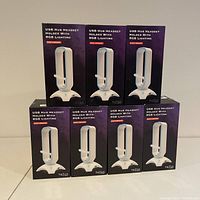 Front view of seven boxed Tilted Nation TNShadow RGB headset stands stacked in pyramid formation, showing product name, image, and features on boxes.