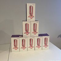 Pyramid stack of 8 Tilted Nation headset stand boxes on white surface, front view showing pink stands with lighting and mouse bungee.