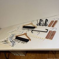 Multiple types of closet hangers and accessories arranged on a white tabletop including plastic hangers, wooden hangers, clip hangers, tie holders, and hat holders.