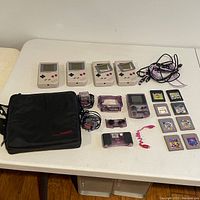Overhead view of entire lot on white table: four DMG-01 consoles, Game Boy Color, carrying case, accessories, cables, and game cartridges.