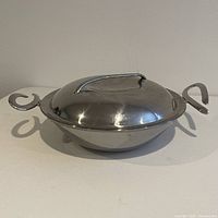 Nambe CookServ 15" stainless steel stir fry pan with lid closed, showing pan shape and handles.