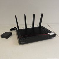 Front and side view of the black Netgear Nighthawk X4S router with four antennas and power adapter cable visible.
