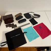 Photo showing five hard sunglass cases, Gucci box, and multiple branded soft bags laid out on a white surface.