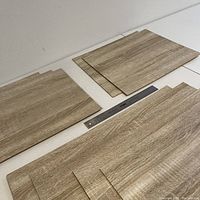 Nine wood style veneer panels laid out on a table with a ruler for scale. Panels show a light wood grain finish in rectangular shapes.