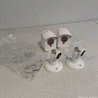 Two outdoor camera housings, two adjustable wall mounts, and packaged mounting hardware displayed on white surface.