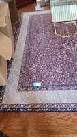Partial top-down view of the area rug showing detailed floral patterns and two-tone border near furniture and hardwood floor.