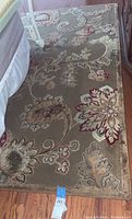 Overall view of taupe floral paisley area rug on hardwood floor under bed