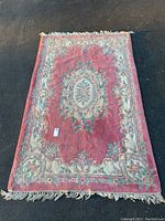 Top view of rectangular area rug with central medallion and floral design in red tones and cream fringe edges