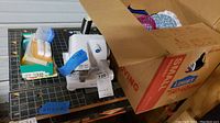 Baby Lock Pro Line sewing machine with spool of thread and parts visible beside cardboard box containing more items.