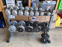 Front view of a two-tier metal dumbbell rack loaded with eight fixed hex dumbbells on top tier and four adjustable dumbbells on lower tier.