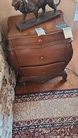 Photo showing entire wooden 3 drawer corner cabinet with curved drawer fronts and ornamental legs, medium brown color. Not including items on top.