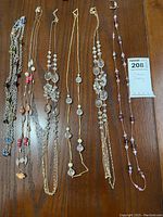 Six costume jewelry necklaces laid flat on wooden surface showing variety in bead colors, chain styles, and lengths.