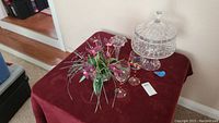 View of full lot on red cloth including cake stand, wine glasses, and floral vase