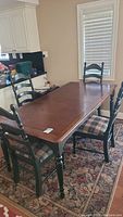 Dining table with four chairs around it on a patterned rug in a room with white cabinets and window blinds.