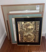 Four framed artworks stacked with front showing a vintage world map print with gold tones and black background