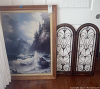 Full view of the framed seascape wall art and two metal decorative panels side by side on floor against wall