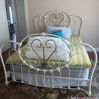 Front view of metal bed frame with headboard and footboard, Sleep Number mattress with yellow foam topper, pillows, and comforter.