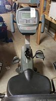 Front view of Schwinn exercise bike showing seat, pedals, handlebars, and digital display screen with buttons below.