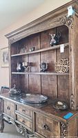 Full view of wooden hutch with metal service trays, teapot, and pitcher displayed on shelves and countertop.