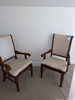 Pair of two upholstered high back chairs with wooden frames and cream diamond quilted upholstery shown side by side against white wall.
