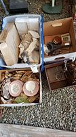 Four boxes of vintage dishes, figurines, and decorative items including plates, trays, and metal ornaments, shown packed with brown paper.